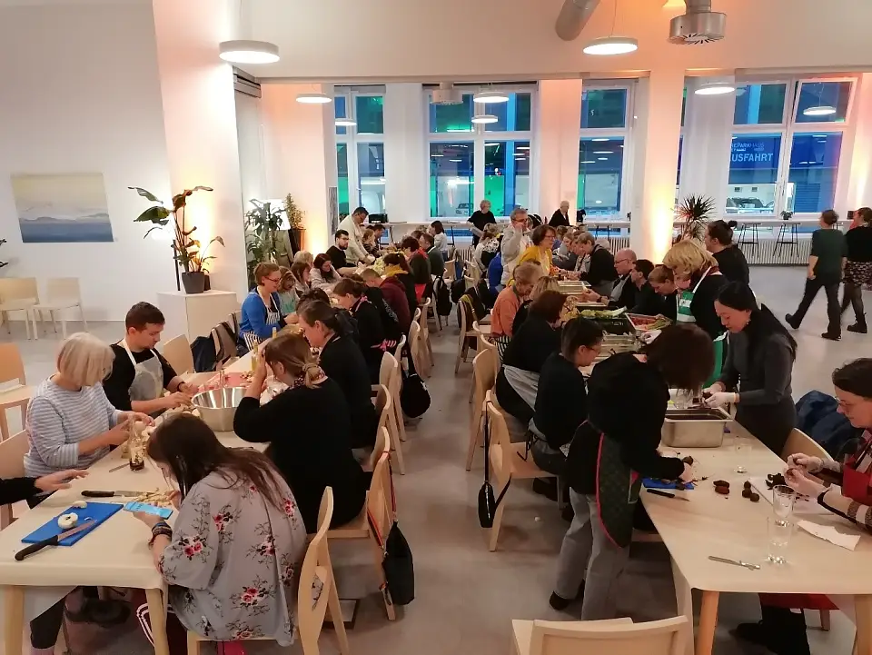 Das Bild zeigt eine Veranstaltung im Forum Küche, bei der viele Menschen gemeinsam an Tischen Lebensmittel vorbereiten.