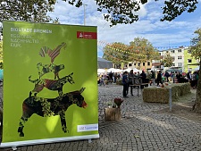 Das Bild zeigt das Banner der BioStadt Bremen mit einer Darstellung der Bremer Stadtmusikanten. Im Hintergrund ist das Marktgeschehen auf dem Bio-Marktfest 2023 zu sehen.