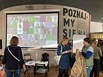 Das Bild zeigt eine Infotafel auf dem Projekttreffen in Gdynia und Besucher:innen