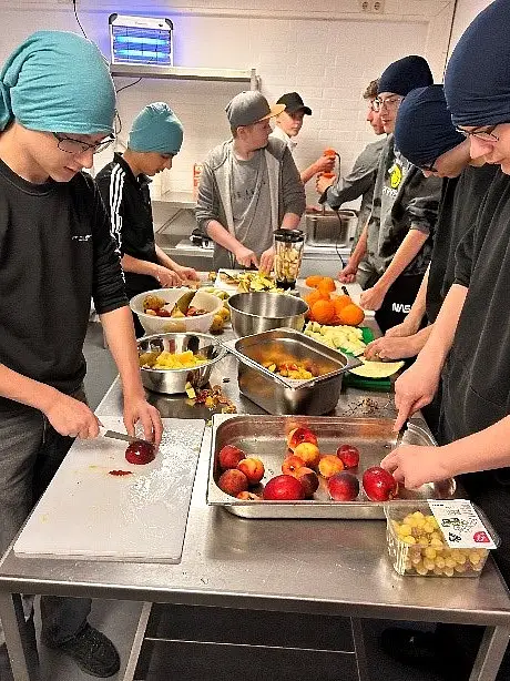 Das Foto zeit eine Gruppe von Jugendlichen, die gemeinsam in einer Küche Obst schneiden.