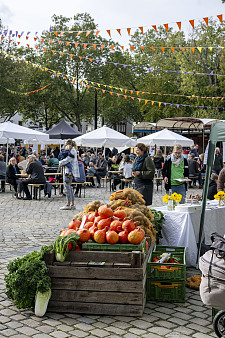 Das Bild zeigt eine lebendige Szene vom Bio-Marktfest. Im Vordergrund ist farbenfrohes Gemüse zu sehen.