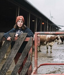 Cover Fotobroschüre: Eine Frau lehnt an einem Zaun und im Hintergrund sind Kühe zu sehen.