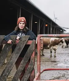 Cover Fotobroschüre: Eine Frau lehnt an einem Zaun und im Hintergrund sind Kühe zu sehen.