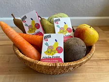 Schale mit Karotten, Kiwis und Äpfeln; dazwischen liegen verteilt Saisonkalender.