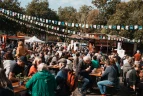 Besucher:innen des Biomarktfests sitzen gemeinsam an Bierzeltgarnituren und genießen die entspannte Atmosphäre.