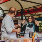 Das Bild zeigt eine Live-Cooking-Szene, bei der die Senatorin Kathrin Moosdorf gemeinsam mit Steffen Rösemeier vom Forum Küche kocht. Die Senatorin trägt eine weiße Kochschürze mit den Logos BioStadt Bremen und Forum Küche. 