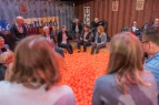 Mehrere Personen sitzen in einem Kreis mit ihren Füßen in einem Bällebad mit orangen Bällen und hören einer Person zu. 
&tilde; Bildnachweis: Christian Arne de Groot