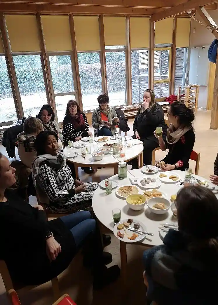 Fortbildung K&uuml;chenfachkr&auml;fte: Das Bild zeigt eine Gruppe von K&uuml;chenfachkr&auml;fen, die um zwei Tische herum sitzen und ihre selbstgemachten Snacks probieren..