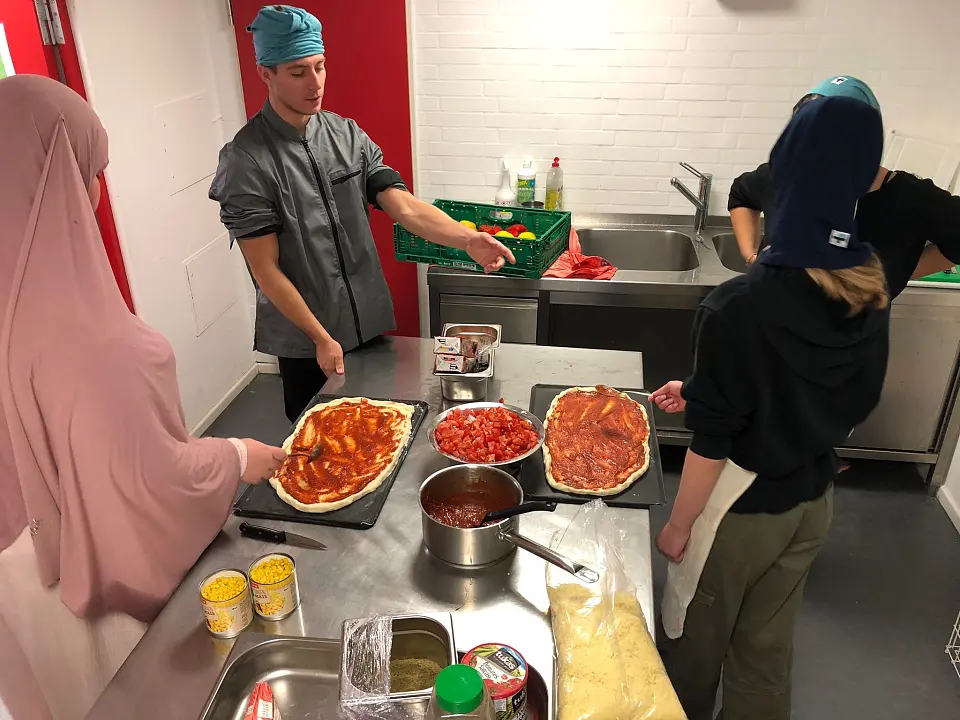 Das Foto zeigt Jugendliche, die unter Anleitung Pizza zubereiten.