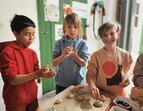 Mit viel Freude und Konzentration formen drei Kinder ihre eigenen Brötchen. Der Teig wird mit den Händen geformt, Körner werden gestreut.  
˜ Bildnachweis: Verein Sozialökologie e.V.