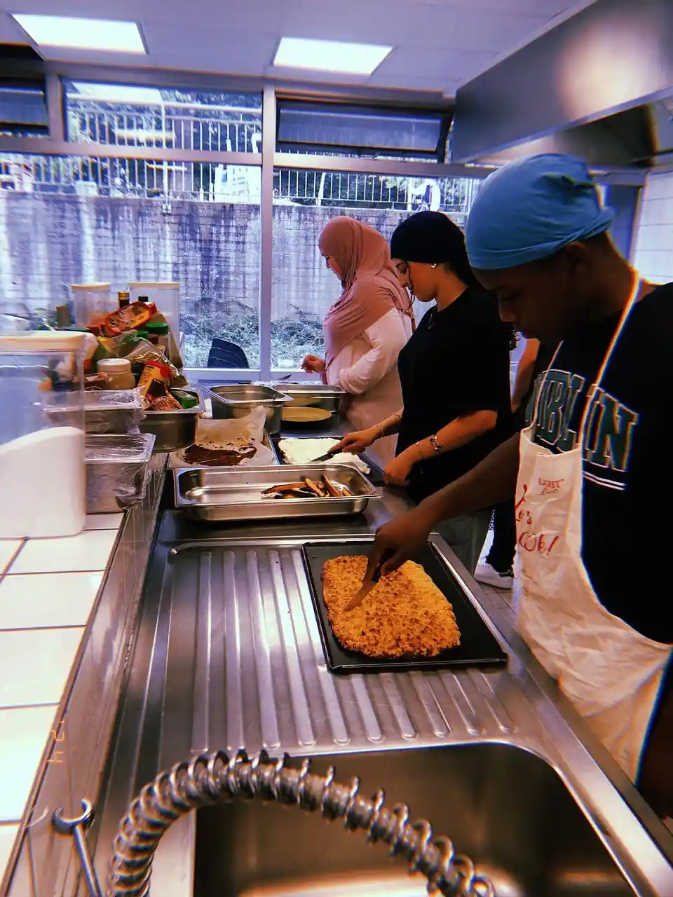 Dieses Foto zeigt drei Jugendliche, die in einer K&uuml;che gemeinsam Speisen zubereiten.